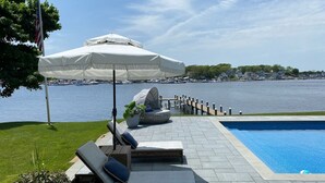 A poolside area with lounge chairs, a covered umbrella, and a view of the water. - Spectacular Riverfront Property (Manasquan)