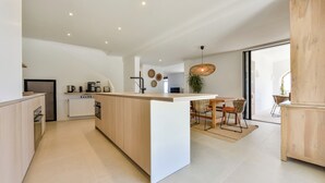 A modern kitchen with a central island, built-in appliances, and a dining area with wicker chairs. - Mirador - By Almarina Villas (Benissa)