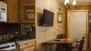 A compact kitchen with wooden cabinets, a stove, a sink, and a television mounted on the wall. - Enjoy beautiful lake view sunsets from the balcony in Room 16 - Angler's Retreat - Curriers Lakeview (Rice Lake)
