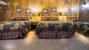 A wooden cabin-style room with three beds, each with a plaid bedspread and a headboard. There are framed pictures on the wall and a lamp on each nightstand. - Enjoy beautiful lake view sunsets from the balcony in Room 16 - Angler's Retreat - Curriers Lakeview (Rice Lake)