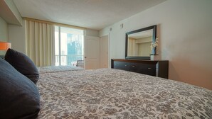A hotel room with a large bed, a dresser, a mirror, and a window with curtains.