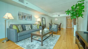 A modern living room with a grey sofa, a coffee table, and a dining area with a wooden table and chairs.