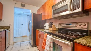 A kitchen with a refrigerator, microwave, stove, and oven. There is a door leading to another room.