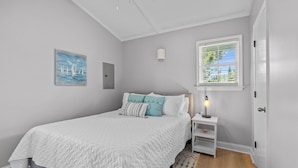Ein Schlafzimmer mit Bett, Nachttisch, Lampe, einem Fenster mit Jalousien und einem Bild an der Wand.