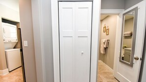 A hallway with a white door, a laundry area, and a bathroom with towels and a mirror. - SweetiePie Studio in the Heights-Steps from Everything! (Peoria Heights)