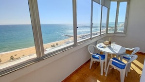 A room with large windows overlooking a beach, a small round table with chairs, and a bottle of wine on the table.