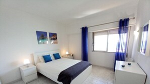 A bedroom with a bed, nightstands, a dresser, and a window with curtains.