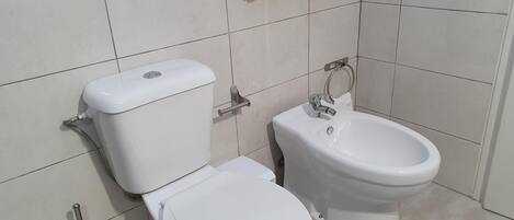 Een badkamer met toilet en bidet, beide wit, inclusief een toiletborstel en een handdoekhouder aan de muur.