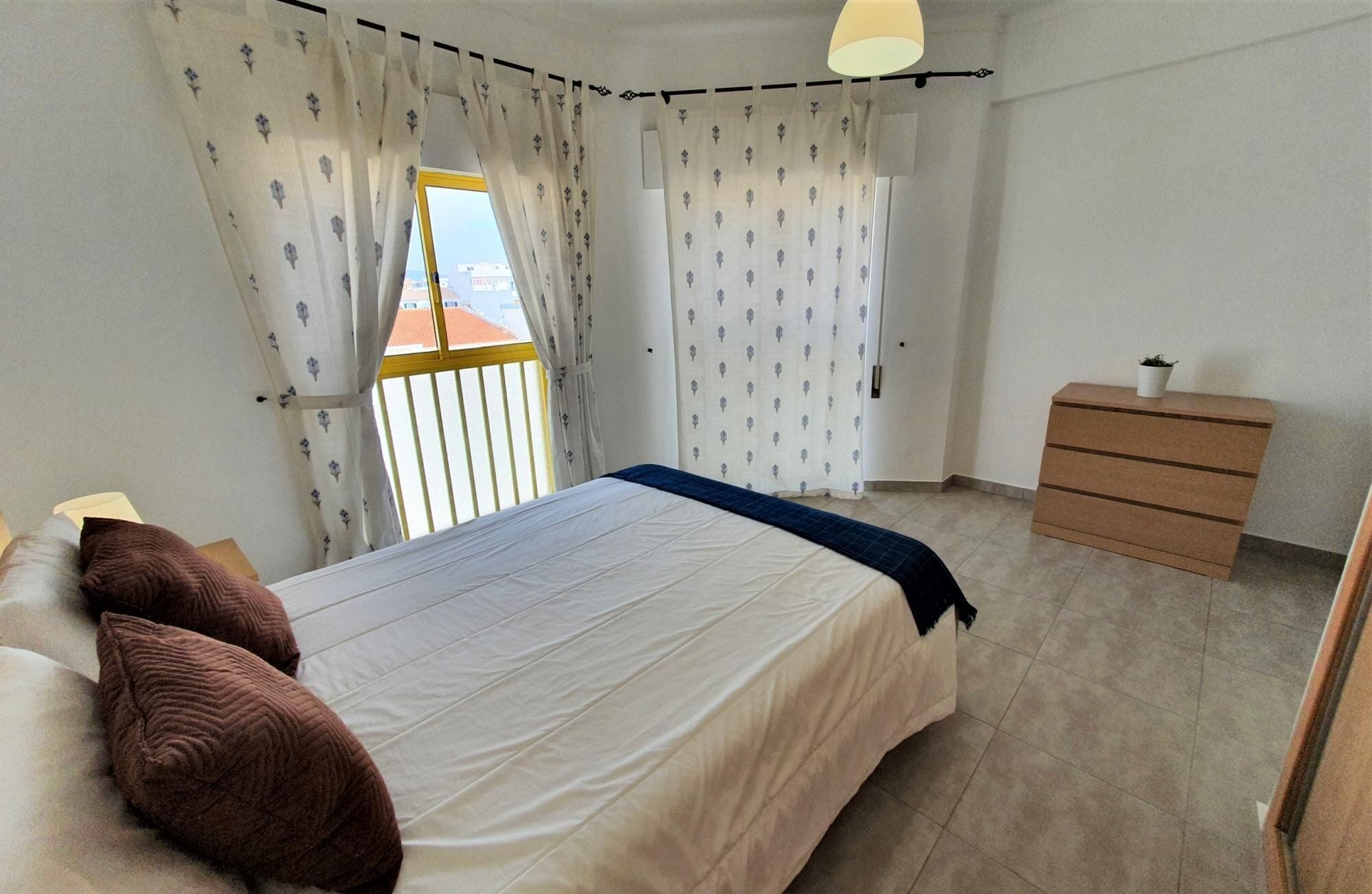 A bedroom with a bed, a dresser, and a window with curtains.