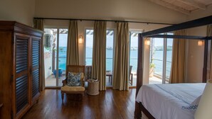 Un dormitorio con una cama grande, una silla con cojín, un armario de madera y vistas al mar a través de amplios ventanales.