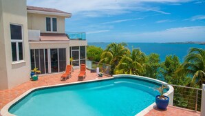 Una casa moderna con piscina, balcón con sillones de descanso y vista al océano.