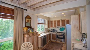 Cocina rústica con armarios de madera, una estufa y una ventana con vistas a la vegetación.