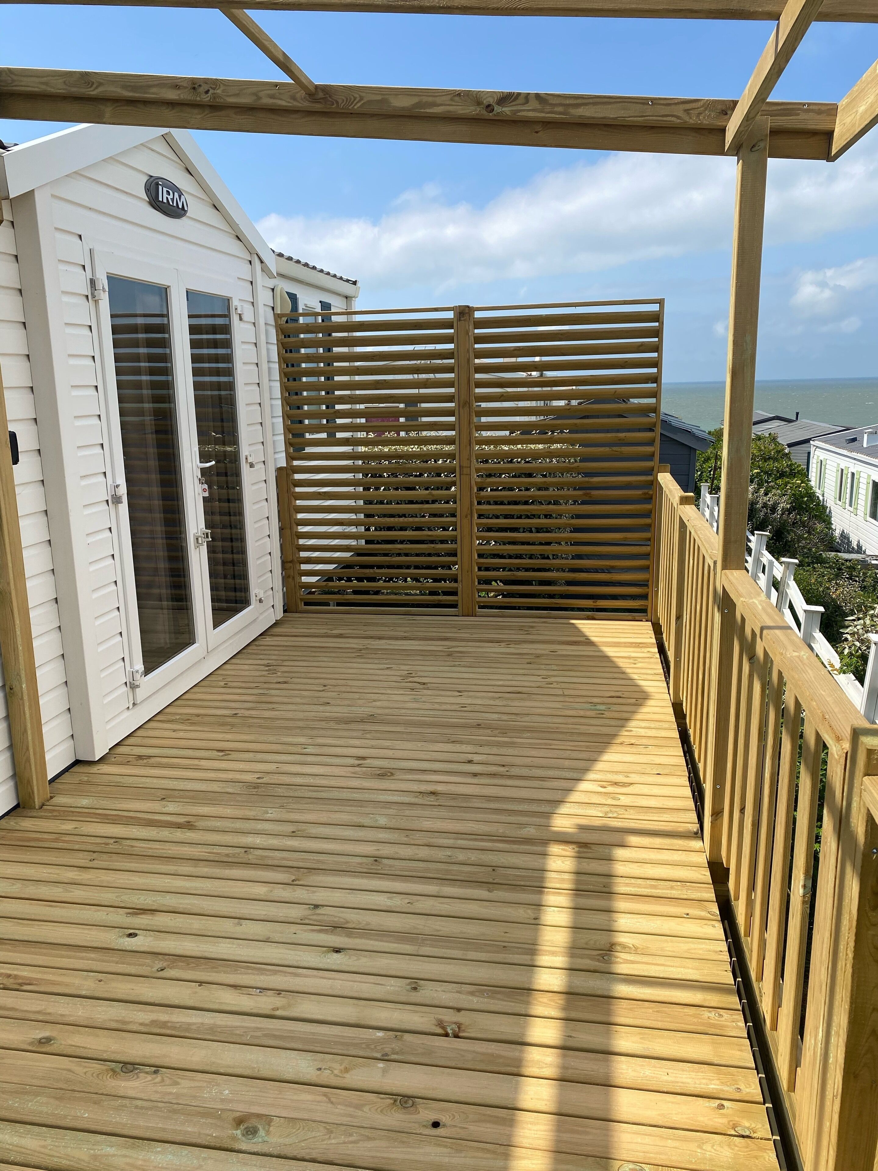 A wooden deck with a view of the sea, a white building with an 'IRM' sign, and a wooden fence.