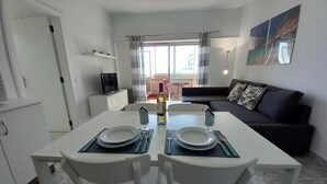 A dining area with a table set for two, a sofa, and a balcony view. - T1 Torre Azul 11 Vista MAR Fabuloso P R DO SOL WI- (Loulé)