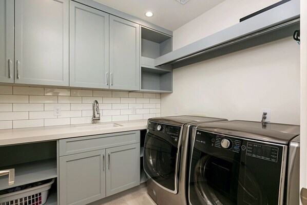 A laundry room with two stacked front-loading washing machines, a sink, and light grey cabinets.