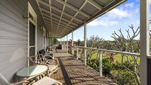 Relax on the covered deck with a view of the surrounding landscape, featuring a wooden deck, wicker chairs, and a small table.