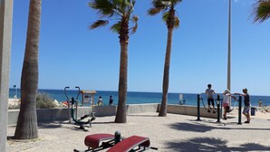 A beachside exercise area with stationary bikes, a red lounge chair, and palm trees. - T0 A C Varandas Mar 3 B Perto Praia Wi-fi (Loulé)