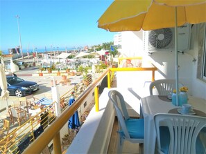 A balcony with a yellow umbrella, a table with chairs, and a view of the street and buildings. - T1 Praiamar Frente MAR A C Estacionamento Wifi (Loulé)