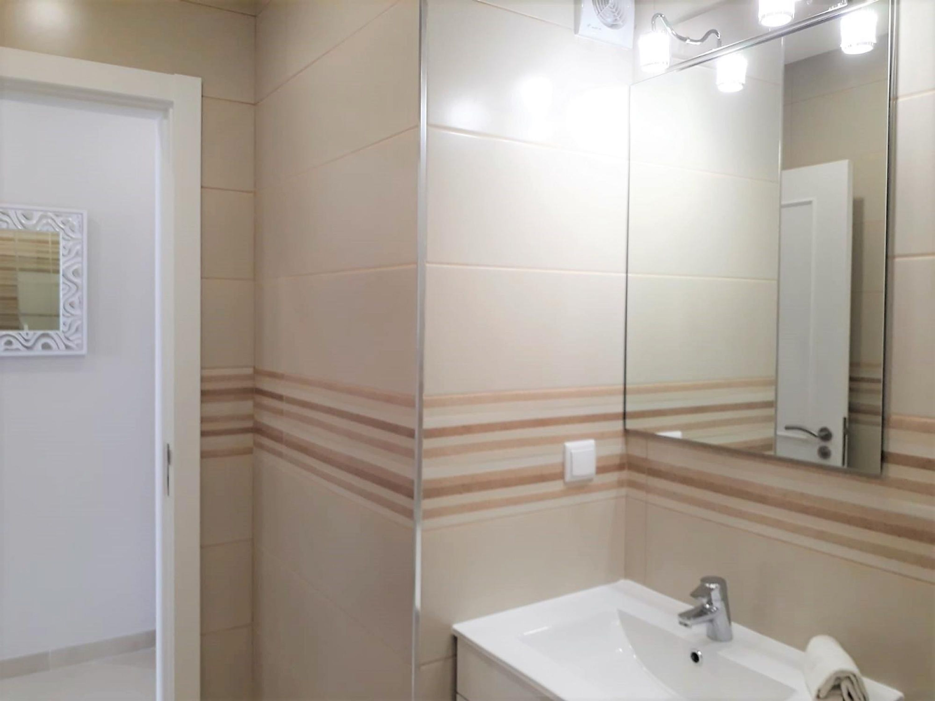 A bathroom with a white sink, a mirror, and striped wall tiles.