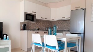 A modern kitchen with white cabinets, a microwave, and a refrigerator. There is a dining table with two chairs and a vase on it. - T1 Praiamar Frente MAR A C Estacionamento Wifi (Loulé)