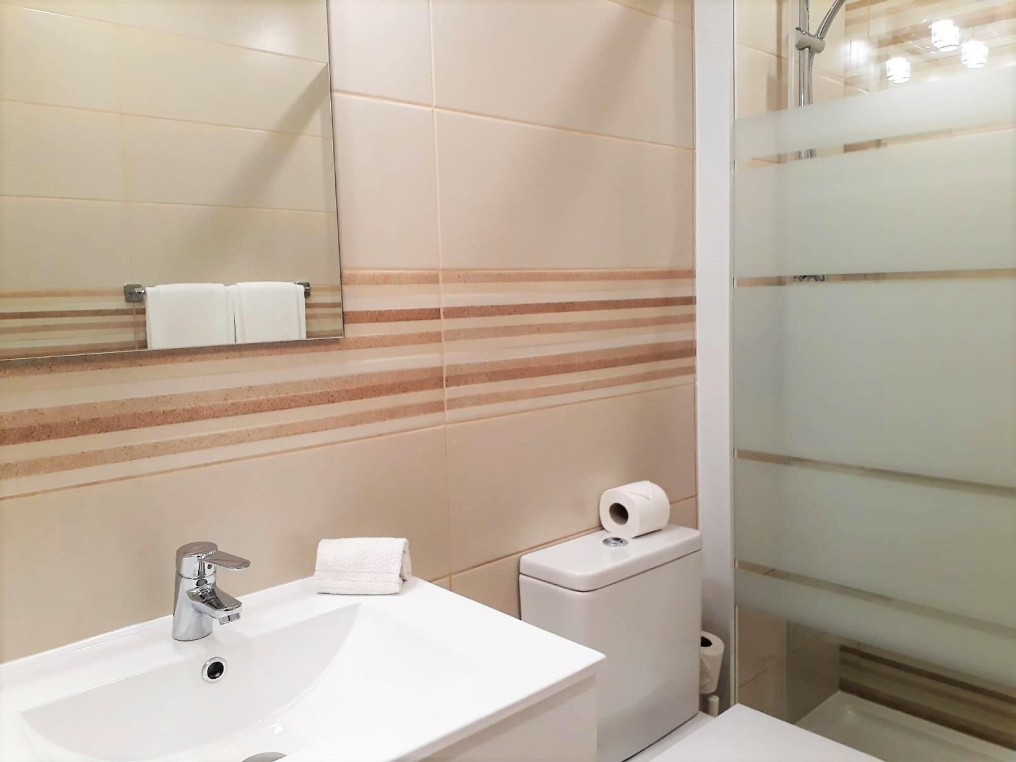 A modern bathroom with a white sink, a mirror, a towel rack, a toilet, and a shower area.