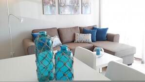 A modern living room with a sofa, blue and white cushions, a coffee table, and decorative vases. - T1 Praiamar Frente MAR A C Estacionamento Wifi (Loulé)