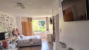 A bedroom with a bed, bedside table, dresser, and a TV mounted on the wall. - Cosy Axminster Studio with Extra Beds (Axminster)