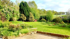A garden patio with a table and chairs, surrounded by lush greenery and a variety of plants. - Cosy Axminster Studio with Extra Beds (Axminster)