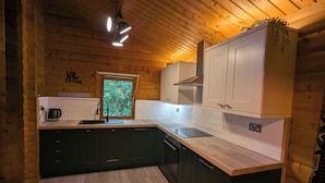 Cocina de cabaña de madera con ventana, gabinetes blancos, encimera negra y alfombra estampada.