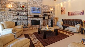 A living room with a stone fireplace, leather sofas, a coffee table, and artwork on the walls. - Beautiful 9-Bed Villa in Gouvia with Tennis Court (danilia)
