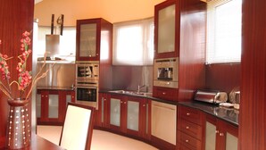 A modern kitchen with wooden cabinets, stainless steel appliances, and a dining area with a table and chairs. - Beautiful 9-Bed Villa in Gouvia with Tennis Court (danilia)