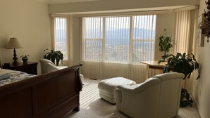 Une chambre à coucher comprenant un lit, une chaise, un bureau et une grande fenêtre donnant sur la ville.