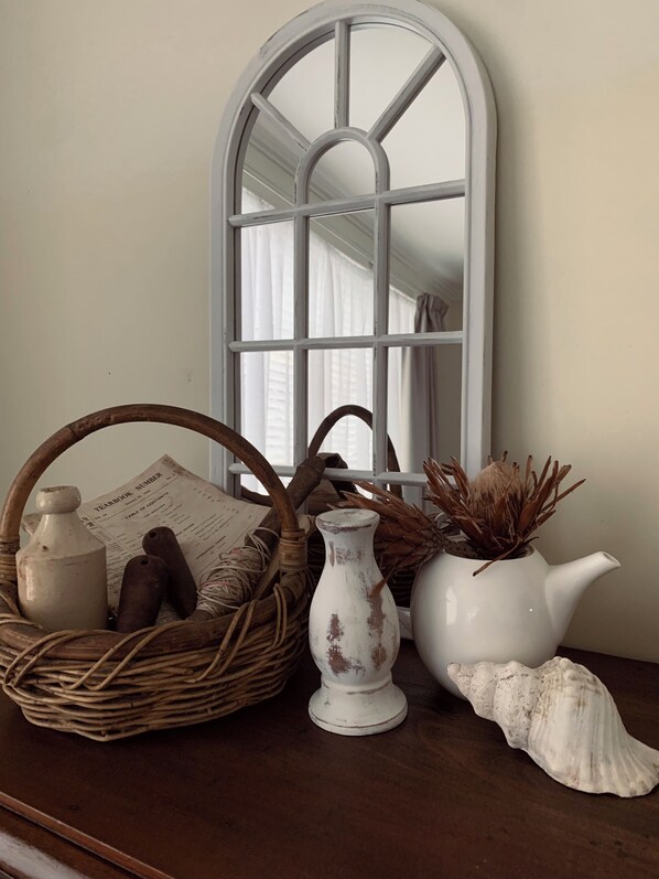 A rustic interior with a wicker basket, a white vase, a potted plant, and a seashell on a wooden surface.