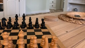 Ein Schachbrett mit Figuren auf einem Holztisch in einem Raum mit Fernseher, Schränken und einer Pflanze.