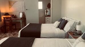Ein Schlafzimmer mit zwei Betten, einem Schreibtisch mit Computer, einem Stuhl, einer Wandkarte und einem Spiegel.