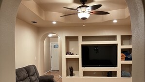 A living room with a sectional sofa, a flat-screen TV, and a ceiling fan. - Villa Maria home is min from Beach, SpaceX, Downtown Brownsville and Matamos Mex (Brownsville)