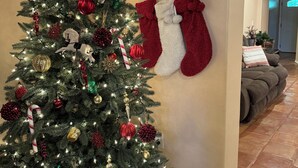 A Christmas tree with red and gold ornaments, a white wall with a decorative panel, and red stockings hanging on hooks. - Villa Maria home is min from Beach, SpaceX, Downtown Brownsville and Matamos Mex (Brownsville)