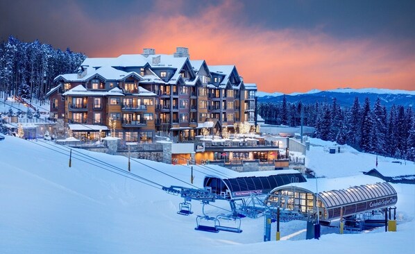Stunning mountain lodge with a central entrance and multiple balconies, offering breathtaking views of the surrounding winter landscape.