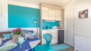 Una cocina compacta con armarios de madera, un comedor con una mesa azul y sillas a juego, y un refrigerador pequeño.