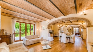 Un vaste salon doté d’un plafond en bois, d’un coin repas et d’une cuisine ouverte sur le salon par une arche.