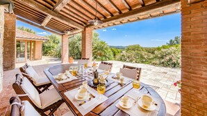 Une terrasse extérieure avec une table en bois dressée pour le repas, entourée de chaises, et offrant une vue sur la verdure et les collines.