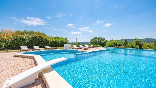 Une piscine entourée de chaises longues, un ciel bleu azur et un paysage vallonné en arrière-plan.