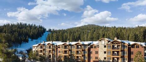 A multi-story lodge with a stone facade, multiple balconies, and a ski slope in the background.