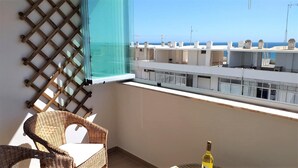 Varanda com cadeira de vime, uma garrafa e vista para o mar e edifícios.