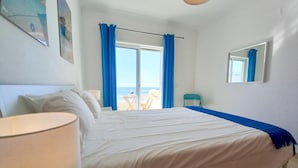A hotel room with a bed, a chair, a table, a window with curtains, and a view of the sea. - T1 Colina Ferias 8C A C Garagem Vista MAR (Loulé)
