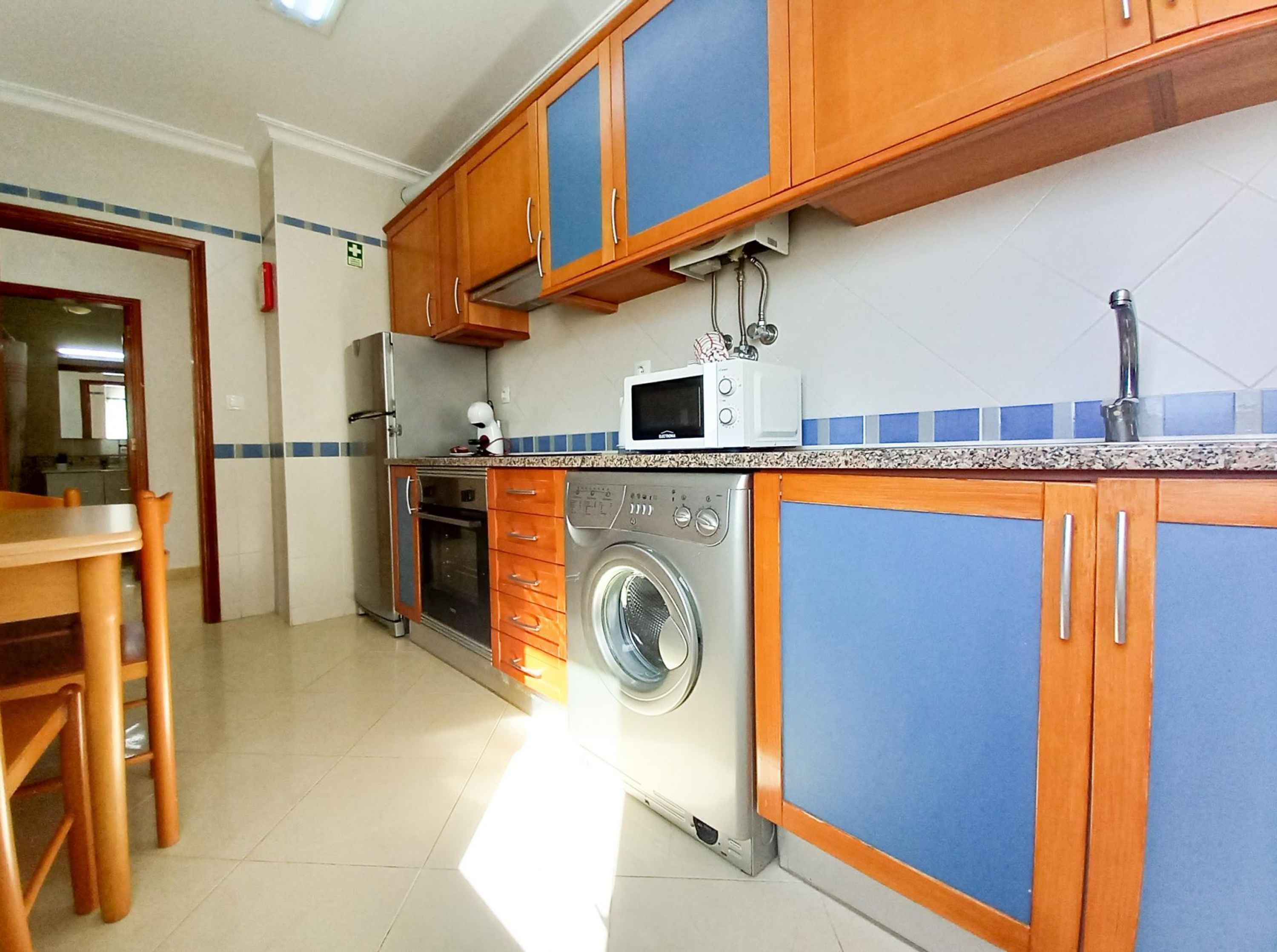 A compact kitchen with wooden cabinets, a washing machine, a microwave, and a sink.