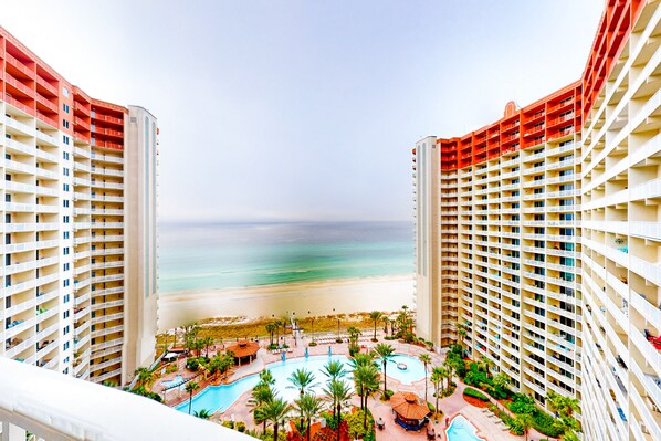 Enjoy breathtaking ocean views from your balcony, overlooking the beach and pool area surrounded by palm trees.