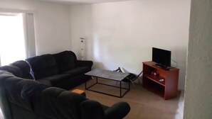A living room with a black sofa, a coffee table, a TV on a wooden stand, and a lamp. - Home away from home! (Decatur)