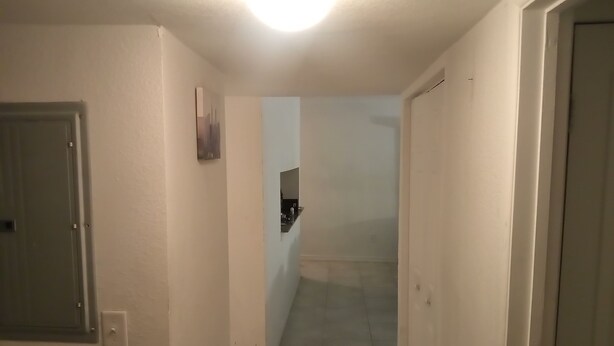 A narrow hallway with white walls and a tiled floor, leading to a room with a visible window. - Home away from home! (Decatur)