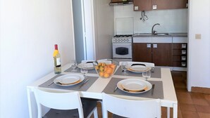 A dining area with a table set for four, a kitchen in the background, and a bottle of wine on the table. - T1 Torre 20 6G M Gico 80M Praia Wi-fi 4 Pessoas (Loulé)